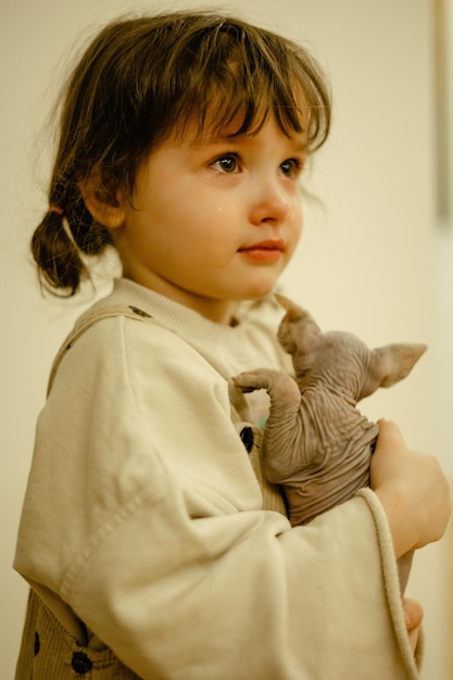 una niña triste y llorona que estaba muy feliz cuando le dieron un gatito esfinge canadiense para que lo sostuviera en sus brazos