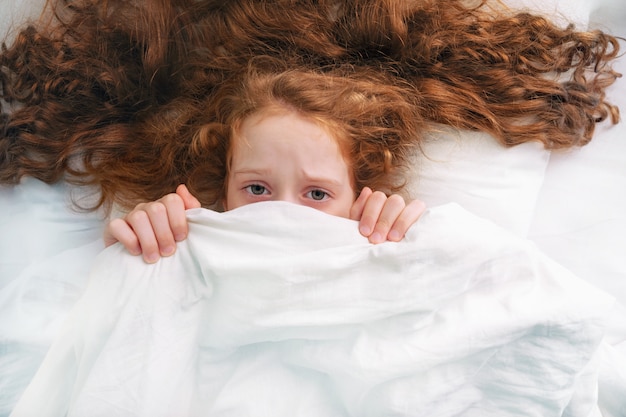 Niña triste miedo dormir y tirar de edredón en la cabeza.