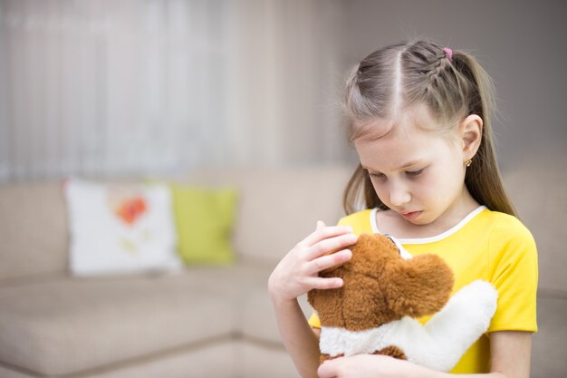 Niña triste con un perro de juguete en casa