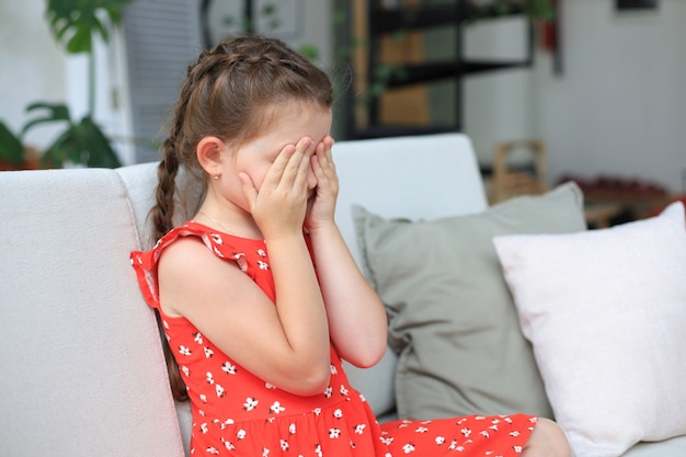 Niña triste sentada en el sofá sola en casa.