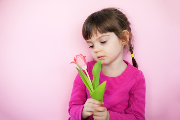 Niña triste en vestido rosa con tulipán rosa