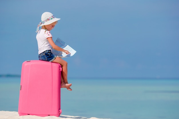 Niña de turistas con maleta grande en tropical playa blanca