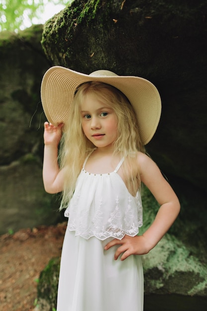 Niña ucraniana de 7 años con cabello blanco como un ángel caminando en el bosque sobre las rocas