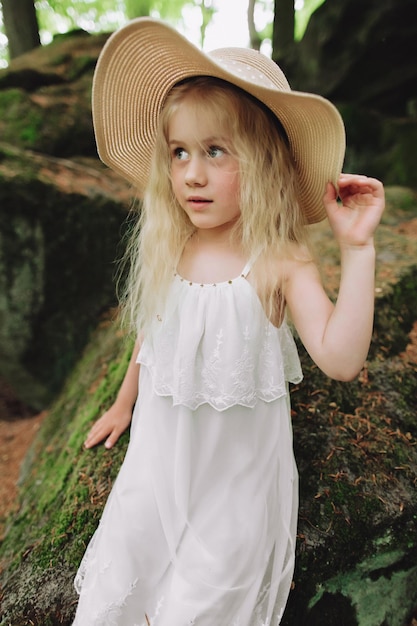 Niña ucraniana de 7 años con cabello blanco como un ángel caminando en el bosque sobre las rocas