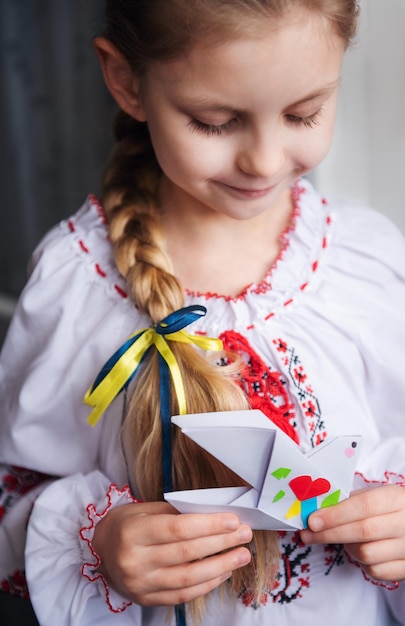 Una niña ucraniana vestida con ropa tradicional sostiene una paloma de paz de papel en sus manos Apoyo a Ucrania Alto a la guerra