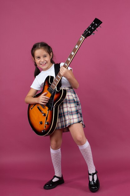 Una niña en uniforme escolar toca una guitarra eléctrica