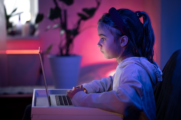 Una niña usa una computadora portátil mientras está sentada en una habitación con luces de neón