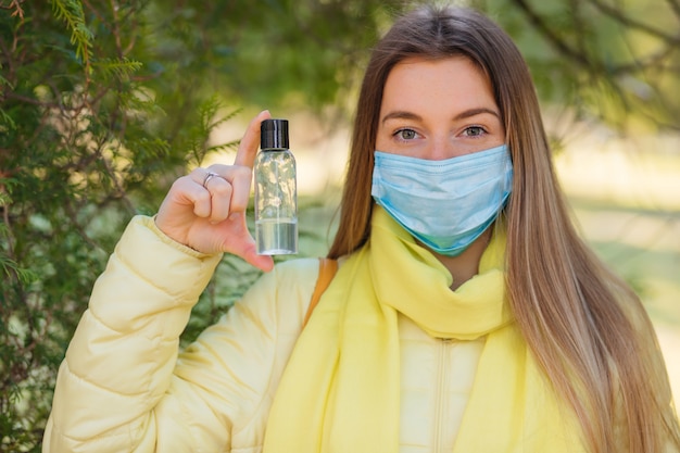 La niña usa una máscara protectora y sostiene una botella de gel antiséptico con alcohol, equipo para desinfección, pandemia de Covid-19, brote de coronavirus, desinfectante de manos para proteger contra enfermedades contagiosas
