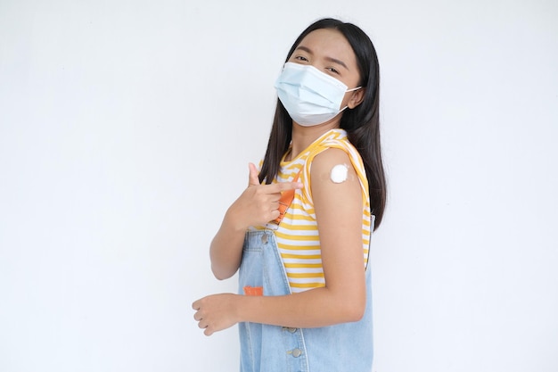 La niña usa una máscara que muestra el brazo después de la vacunación con fondo blanco.