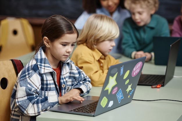 Niña usando una computadora portátil en la mesa de la escuela
