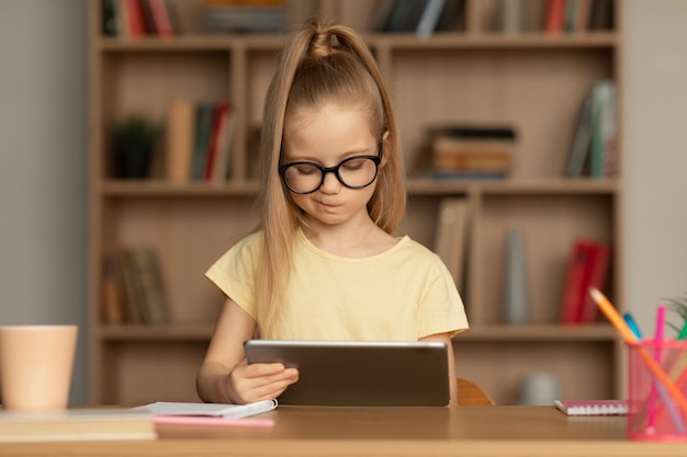 Niña usando tableta digital aprendiendo remotamente sentado en casa