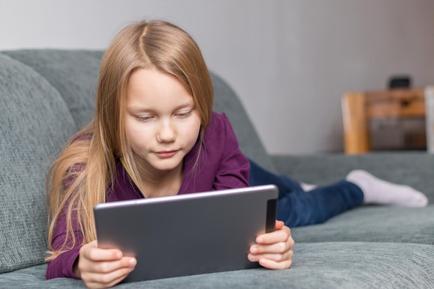 Niña usando una tableta digital en el sofá en casa