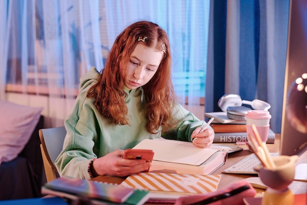 Niña usando teléfono inteligente mientras hace la tarea