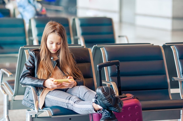 Niña usando teléfono móvil mientras está sentada en el aeropuerto