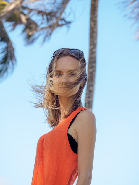 Niña de vacaciones en un chaleco naranja y gafas de sol en una isla tropical. soplando una fuerte brisa del océano