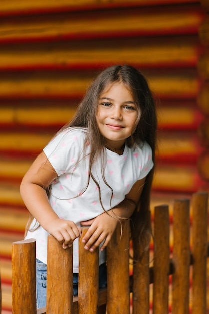 Una niña se para en una valla de madera y se aferra a ella con las manos en verano