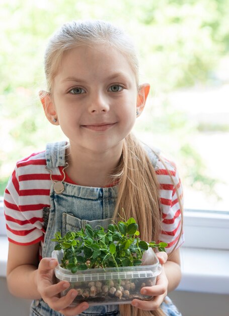 Una niña en la ventana observa cómo crecen los guisantes