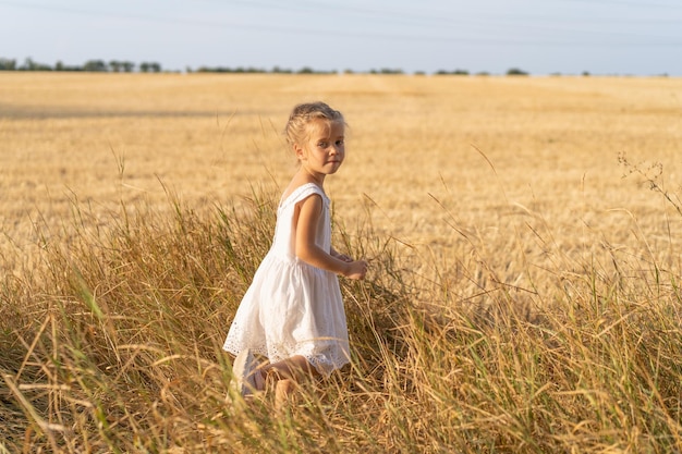 Niña vestida de blanco vestido caminando campo de trigo día de verano