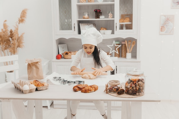 Una niña vestida de cocinera en la cocina prepara galletas.