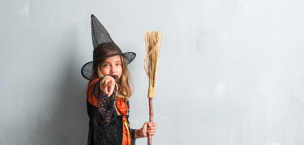 niña vestida como una bruja y sosteniendo una escoba para las vacaciones de halloween apuntando al frente