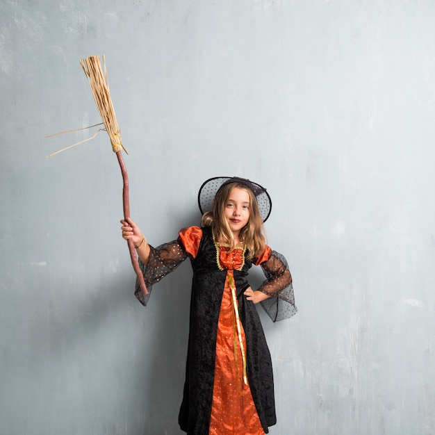 Niña vestida como una bruja y sosteniendo una escoba para las vacaciones de halloween