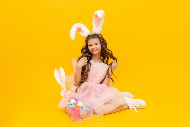 Una niña vestida como un conejito de Pascua con una canasta de huevos coloridos sobre un fondo amarillo aislado Primavera festiva Pascua