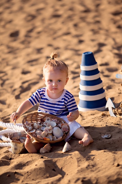 Niña vestida de marinero en una playa de arena con conchas junto al mar