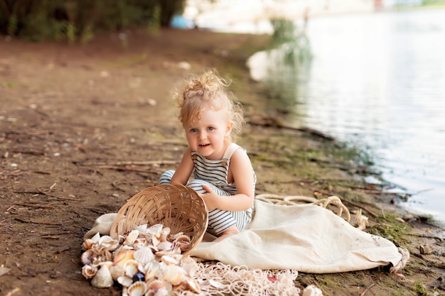 Niña vestida de marinero en una playa de arena con conchas junto al mar