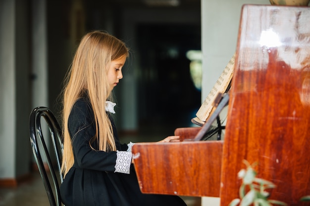 Niña vestida de negro aprende a tocar el piano. El niño toca un instrumento musical.