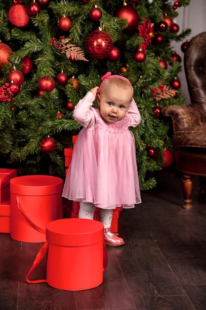 Niña vestida de rosa en el árbol de Navidad decorado de fondo en casa mirando a la cámara