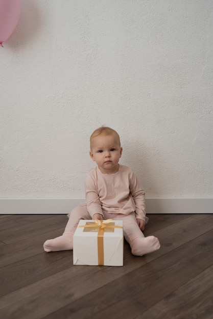 Una niña vestida de rosa con un regalo en un fondo de pared blanca