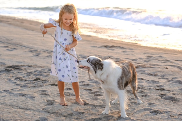 niña vestida de verano juega con una mascota de perro en la playa al amanecer