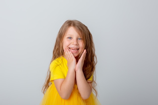 niña en vestido amarillo muestra diferentes emociones fondo blanco feliz