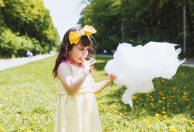 Una niña con un vestido amarillo en un paseo por un parque de atracciones come algodón de azúcar