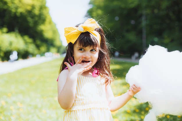 Una niña con un vestido amarillo en un paseo por un parque de atracciones come algodón de azúcar