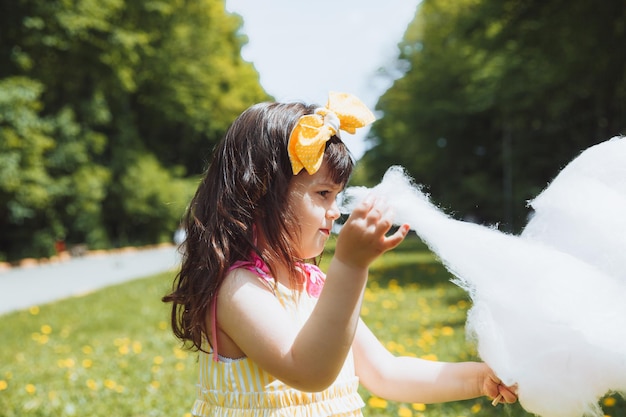 Una niña con un vestido amarillo en un paseo por un parque de atracciones come algodón de azúcar