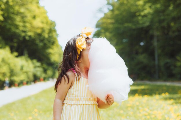 Una niña con un vestido amarillo en un paseo por un parque de atracciones come algodón de azúcar