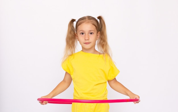 Niña con un vestido amarillo sostiene una pesa y está sentada en un aro. Aislado sobre fondo blanco.