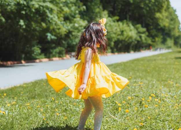 Una niña con un vestido amarillo de verano atrapa burbujas de jabón en la hierba en la corona de dientes de león del parque