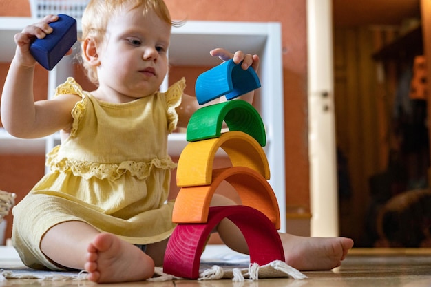Foto niña en vestido de apilamiento de bloques de arco de arco iris edificio torre de juguete de madera ecológica