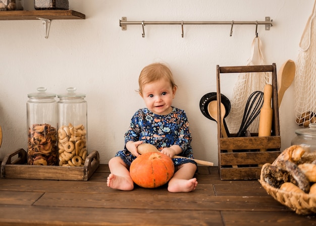 Una niña con un vestido azul está sentada en una cocina de madera