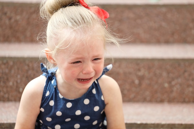 Foto niña con un vestido azul se sienta en los escalones y llora