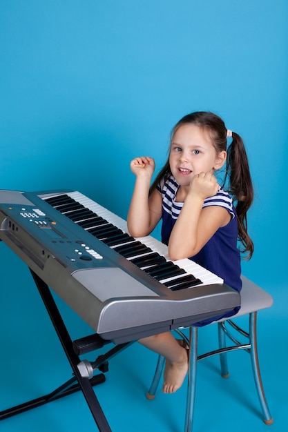 niña con un vestido azul se sienta en una silla y toca el piano con los codos