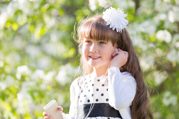 Una niña con un vestido blanco escucha música a través de pequeños audífonos.