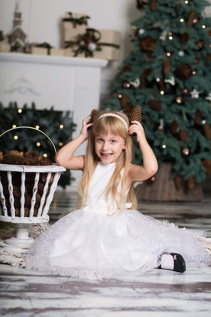 Niña con un vestido blanco juega con piñas en adornos navideños