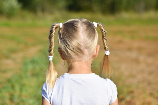 La niña en el vestido blanco mira adelante en el campo, vista posterior, primer plano