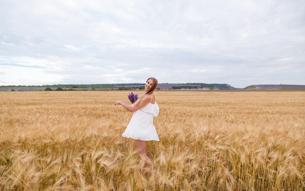 Una niña con un vestido blanco y con un ramo de lavanda en un campo de trigo