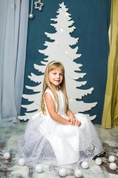 Niña con un vestido blanco se sienta en un soplo con decoración navideña