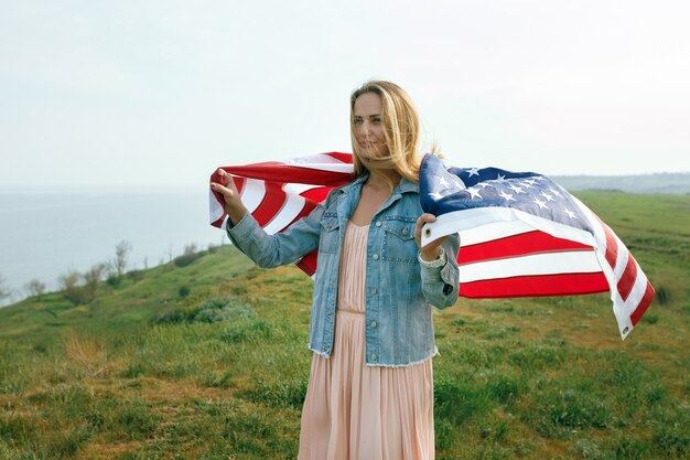 Una niña con un vestido coral y una chaqueta vaquera sostiene en sus manos la bandera de los Estados Unidos. 4 de julio Día de la Independencia.