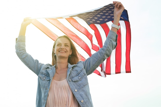 Una niña con un vestido coral y una chaqueta vaquera sostiene en sus manos la bandera de los Estados Unidos. 4 de julio Día de la Independencia.